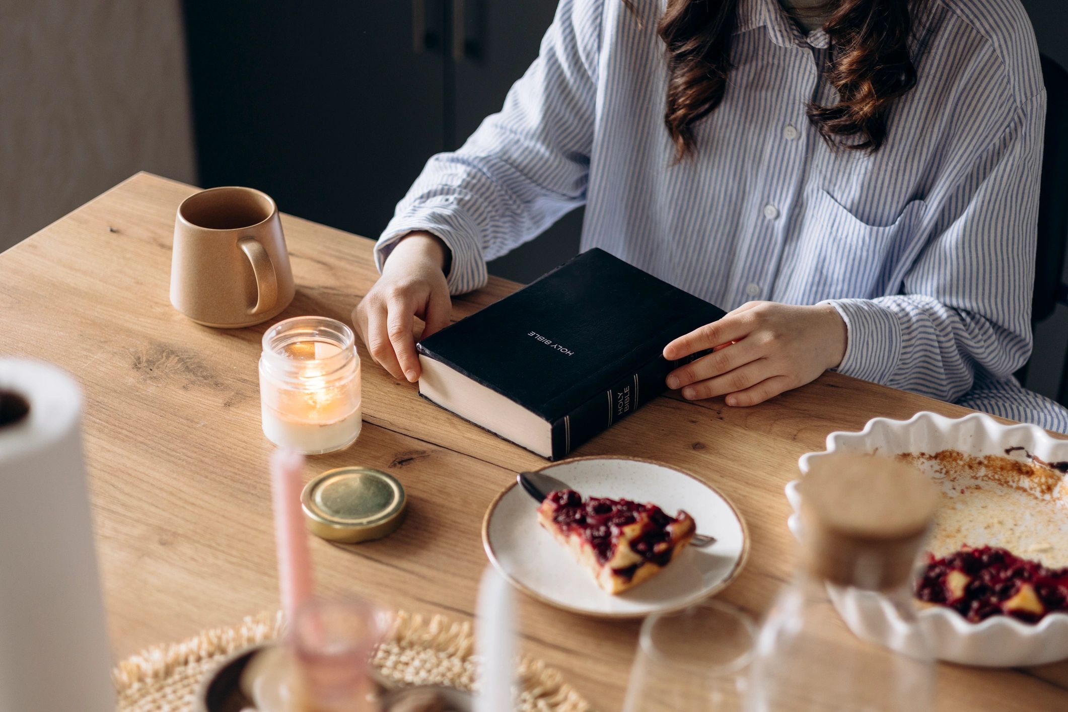 Person reading a Bible at a kitchen table in warm morning light