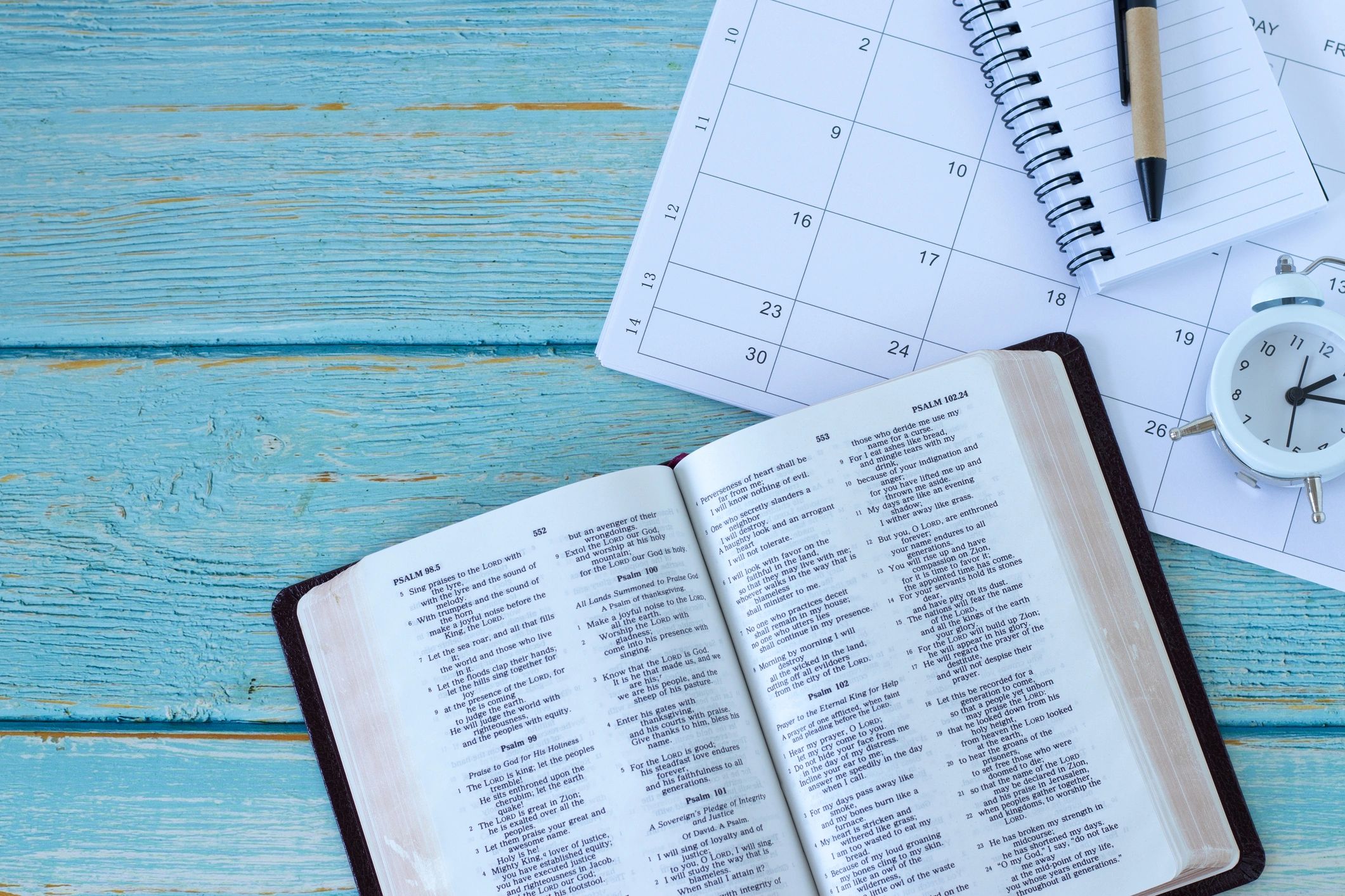 Open Bible with notebook and alarm clock on a desk